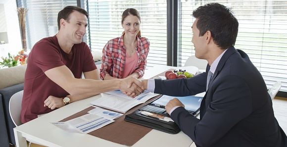 Banker shaking hands with couple in meeting at home.