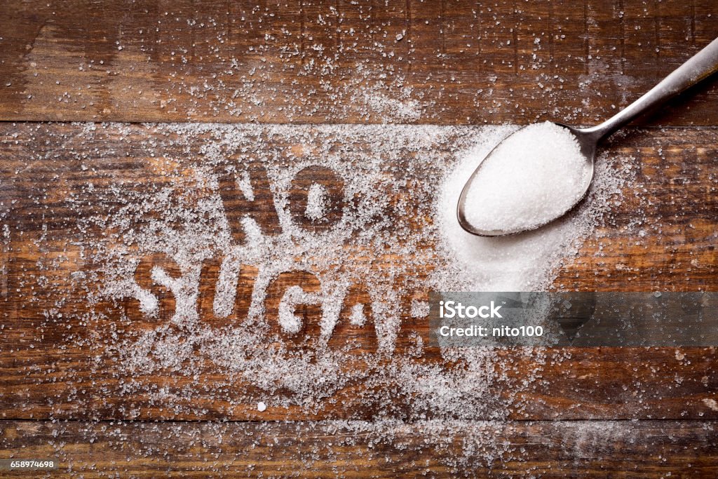 text no sugar written with sugar high-angle shot of a wooden table sprinkled with sugar where you can read the text no sugar and a spoon full of sugar Sugar free Stock Photo