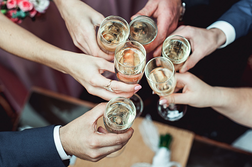 People hold in hands glasses with white wine. wedding party. friends toasting with a champagne above white table