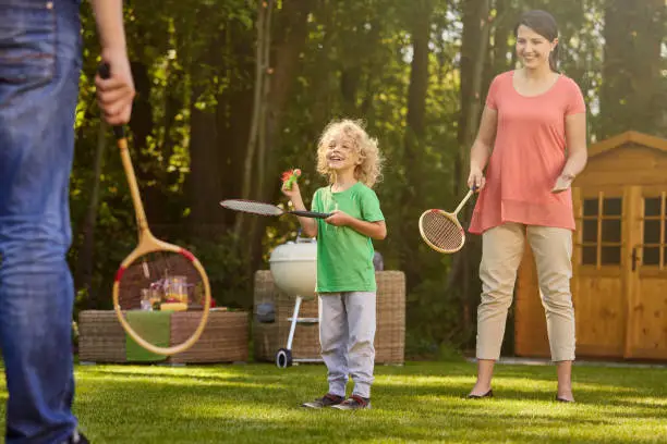 Happy boy playing badminton with parents in garden