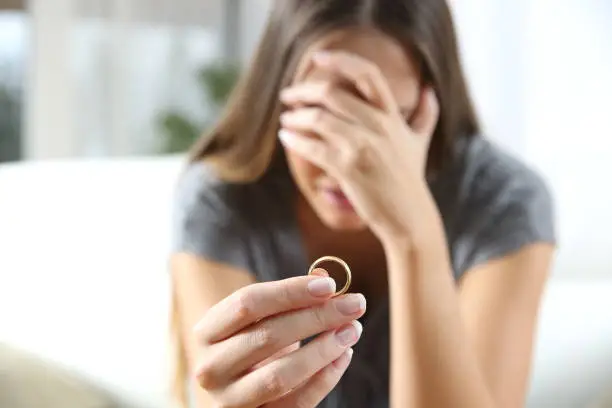 Closeup of a single sad wife after divorce lamenting holding the wedding ring in a house interior