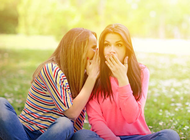istock Two girl friends whispering secrets at park 659111546