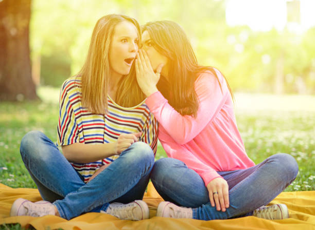 istock Two girl friends whispering secrets at park 659111578