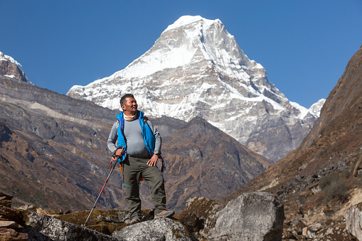 Mature high Altitude Himalaya Nepalese Mountain Guide staying on Rock with Backpack and looking Up