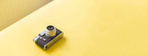 An old analog vintage  camera as a single object on yellow table with big copy space.
