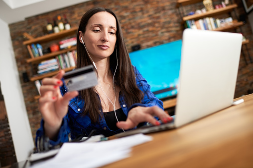 Woman is holding credit card and using laptop computer in order to buy products online.