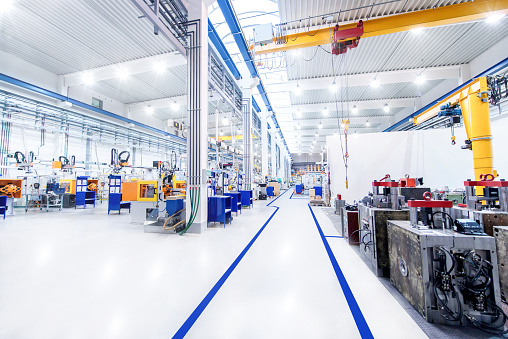 Horizontal image of huge new modern factory with robots and machines producing industrial plastic pieces and equipment. Wide angle view of futuristic machines and long aisle.