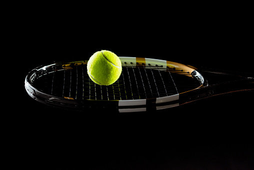 Close-up view of bright tennis ball and racket on black