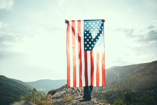 One woman, standing on mountain, holding USA national flag.