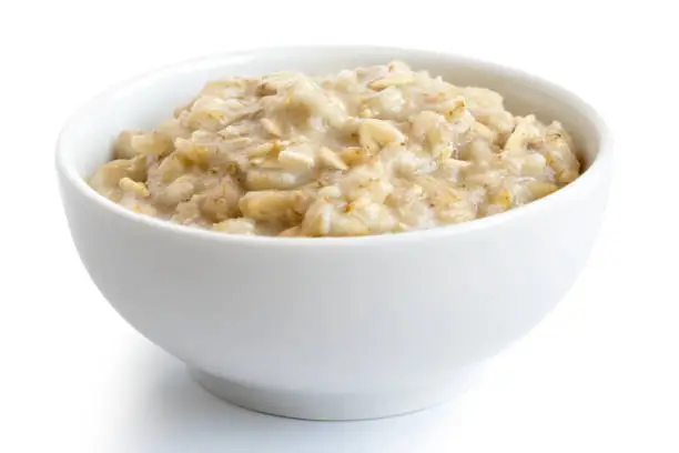 Cooked whole porridge oats in white ceramic bowl isolated on white.