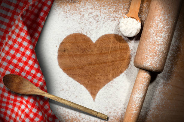 Baking background with a heart of flour on a wooden table with spoons, rolling pin and a red and white checkered tablecloth