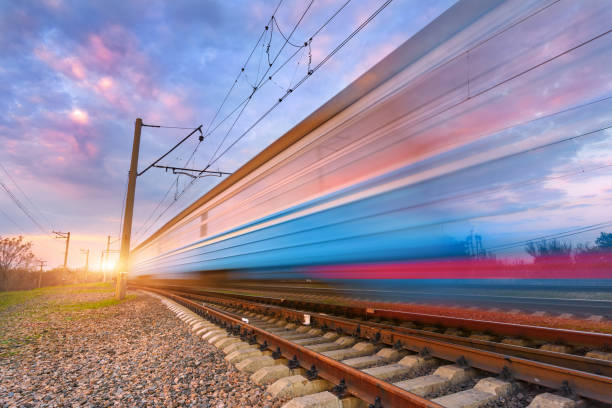 istock High speed blue passenger train in motion on railroad at sunset. Blurred commuter train. Railway station against colorful sunny sky. Railroad travel, railway tourism. Industrial landscape. Concept 659227074