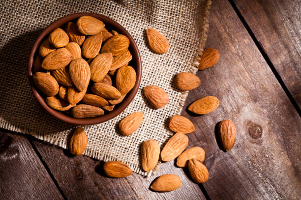 Organic almonds still life Top view of a brown bowl filled with organic almonds shot on rustic wood table. Some almonds are out of the bowl on a burlap. Predominant color is brown. DSRL studio photo taken with Canon EOS 5D Mk II and Canon EF 100mm f/2.8L Macro IS USM Almonds stock pictures, royalty-free photos & images
