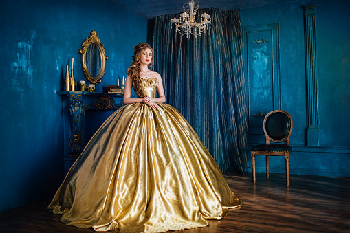 Beautiful woman in a golden ball gown in the great blue interior