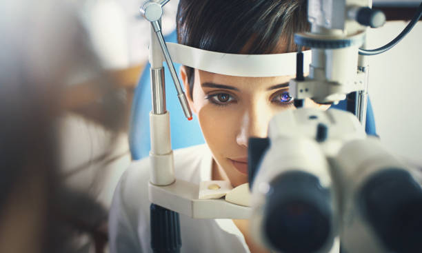 Eyesight exam. Closeup of mid 20's brown eyed woman having her eyes examined at optometrists office. Her head is placed into tomography machine and light beam is shining through her retina and lens. eye test equipment stock pictures, royalty-free photos & images