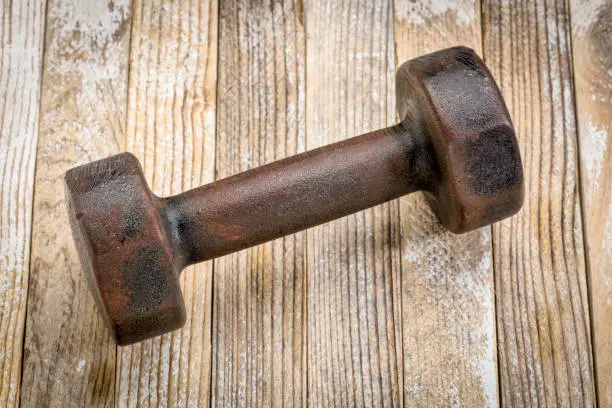 vintage rusty iron dumbbell on grunge white painted wood planks background - fitness concept