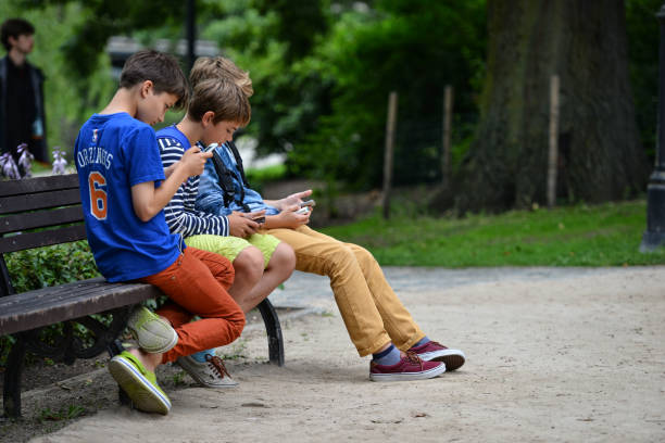 Riga, Latvia - July 27, 2016: Unknown young company sitting on a park bench and in smartphone play Pokemon Go.