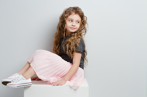 Little girl sitting in pink skirt.