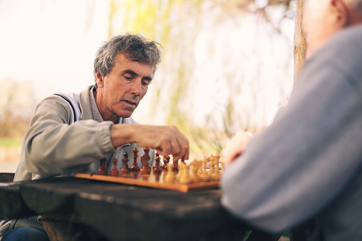 Active retired people, old friends and free time, two senior men having fun and playing chess at park