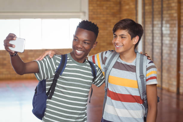 Happy schoolboys taking selfie on mobile phone in campus at school