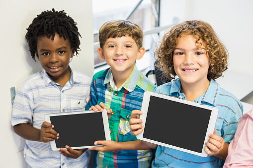 Portrait of smiling students holding digital tablet in classroom at elementary school