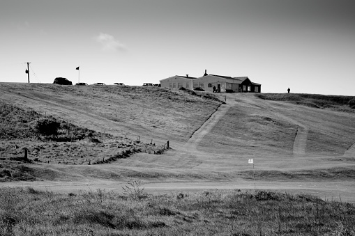 Links golf course with a mature golfer teeing off at the top of the hill beside the clubhouse at Warkworth in Northumberland. The course is beside the public footpath to the beach.