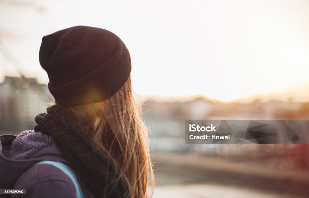 Hipster girl looking at sunset Hipster girl walking on the city street looking at sunset Rear View Stock Photo