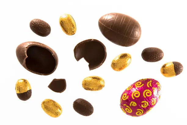 High angle view of a variety of wrapped and unwrapped Easter chocolate eggs on a white background