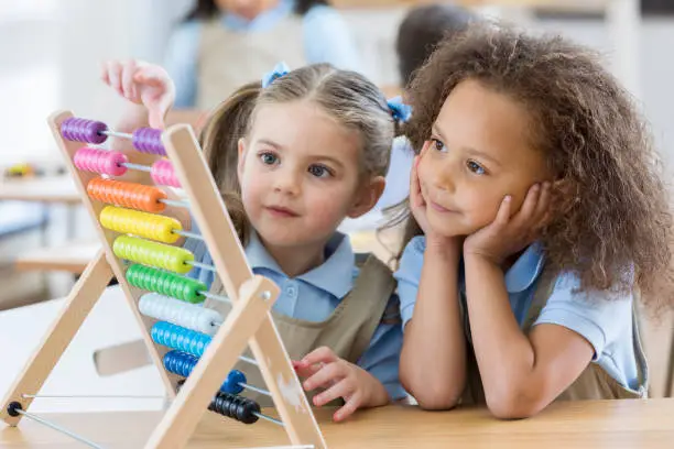 Happy preschool friends enjoy using an abacus during preschool. The students are wearing school uniforms.