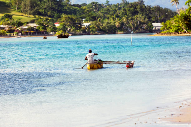 Port Vila, Vanuatu - March 20, 2017: Vanuatu fisherman paddle his outrigger canoe near beach in sunny day. Full frame horizontal composition with copy space