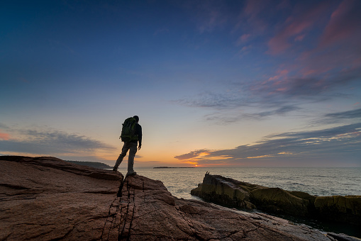 Backpacker standing near the waters edge in Acadia National Park during a sunrise.