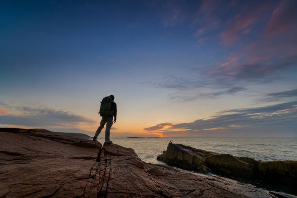 Backpacker watching the sunrise in Maine Backpacker standing near the waters edge in Acadia National Park during a sunrise. maine landscape new england sunset stock pictures, royalty-free photos & images