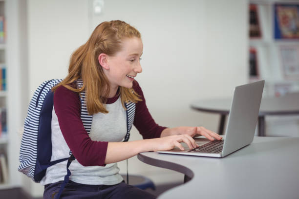 istock Happy schoolgirl with schoolbag using laptop in library 659586684