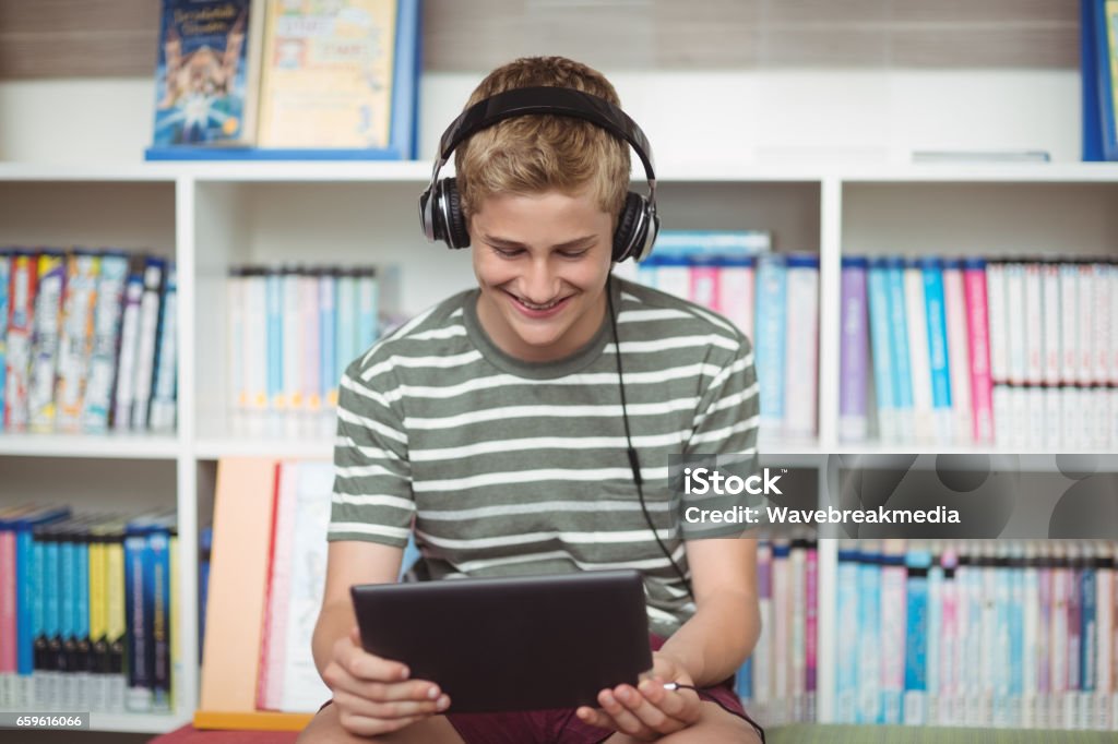 Happy schoolboy listening music while using digital tablet in library Happy schoolboy listening music while using digital tablet in library at school 12-13 Years Stock Photo