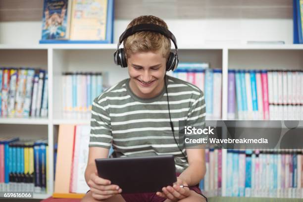 Happy Schoolboy Listening Music While Using Digital Tablet In Library Stock Photo - Download Image Now