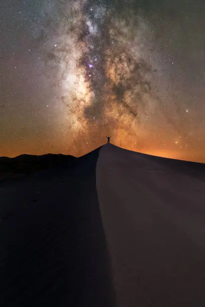 Silhouette of a person standing on a sand dune at Great Sand Dunes National Park under the Milky Way Galaxy.