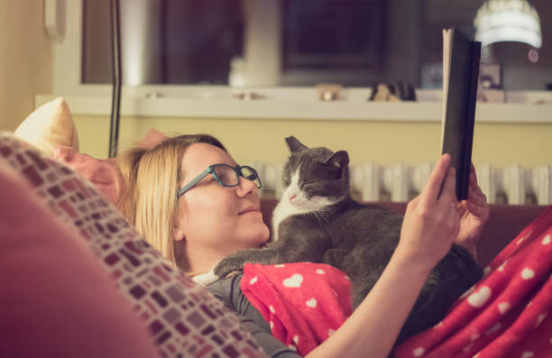 istock Young woman reading a book with her cat at night 659702148