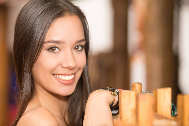 Young lady poses for this close-up portrait. She is smiling, looking at the camera. She is latin, with brown eyes and hair. Her hair is brown, long and smooth. She looks like in her twenties.