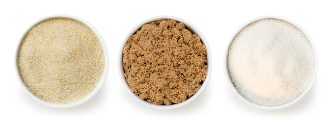 Sugar varieties in small bowls, isolated, top view.  Includes raw, brown, and white.