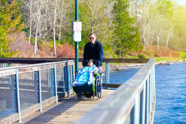 istock Disabled boy in wheelchair walking at park with father 659830358