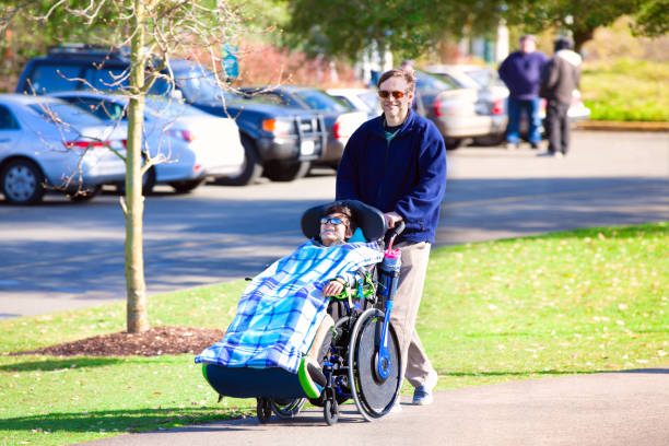 istock Disabled boy in wheelchair walking at park with father 659830556