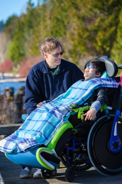 istock Disabled boy in wheelchair talking with father at lakeside park 659830712