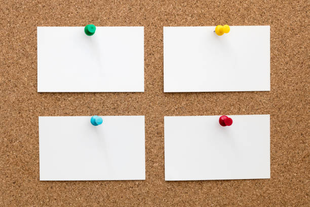 Four blank business cards fastened with push pins on cork board.