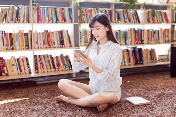 istock Smiling female student using smartphone on carpet in bookshop 659908870