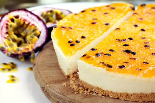 Passionfruit cheesecake, side view on old board.  Focus on front of cheesecake.  Fresh fruit behind.