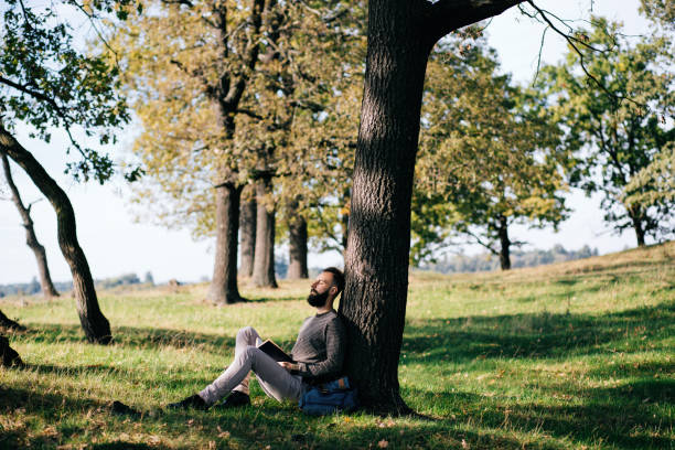 istock Handsome Young bearded student man hipster reading book in park on a summers sunny day 659987650
