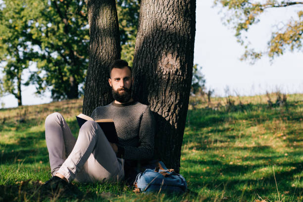 istock Handsome Young bearded student man hipster reading book in park on a summers sunny day 659987794