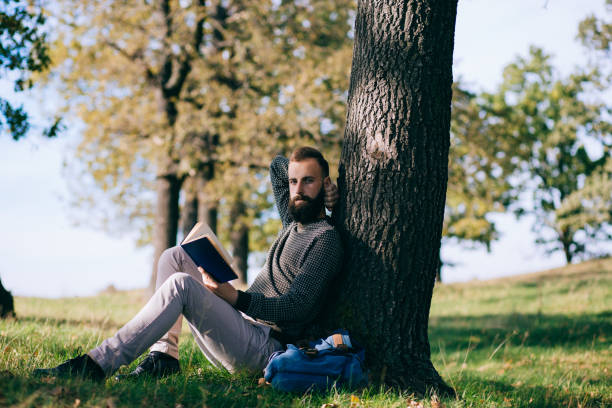 istock Handsome Young bearded student man hipster reading book in park on a summers sunny day 659987826
