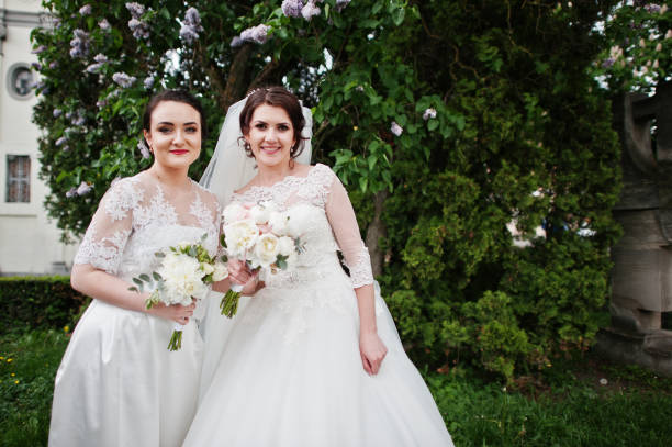 istock Bride with bridesmaid looking at camera near lilac tree. 659988360