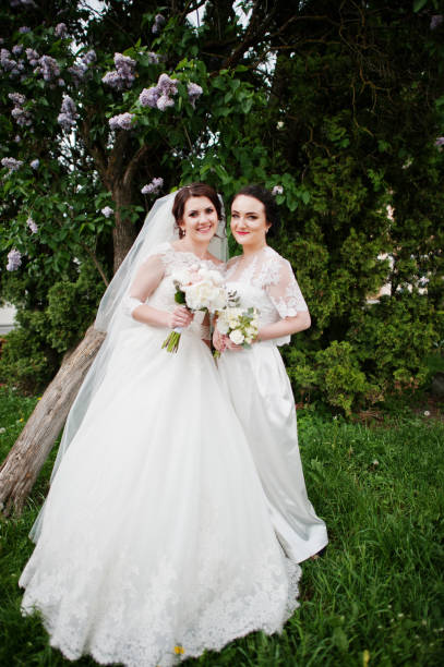 istock Bride with bridesmaid looking at camera near lilac tree. 659988376